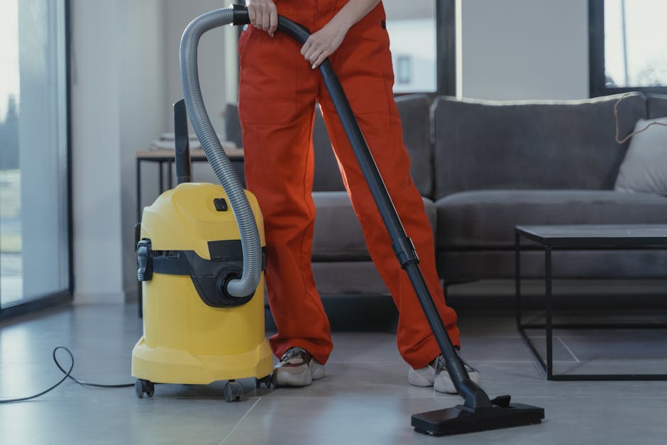 A professional cleaning technician dressed in white protective clothing, including a hood, mask, and gloves, is conducting a deep cleaning process on a carpet in a residential living room. The technic